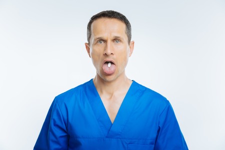 Mature medical worker holding pill on his tongueの写真素材