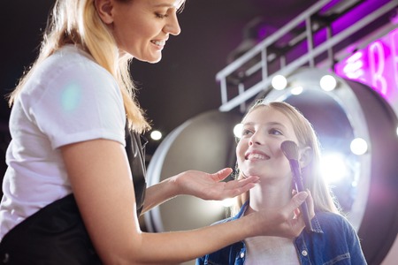 Smiling woman applying makeup to girls faceの写真素材