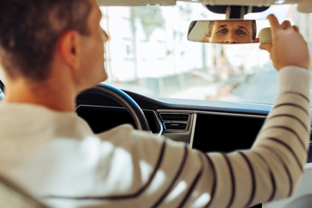Joyful positive man looking into the rear view mirror