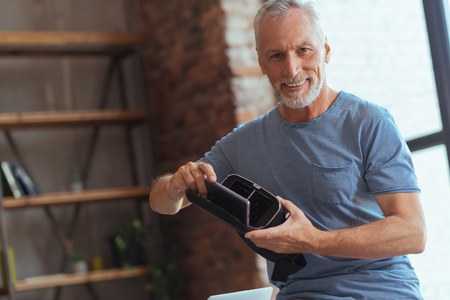 Cheerful aged man holding VR glasses in handsの写真素材