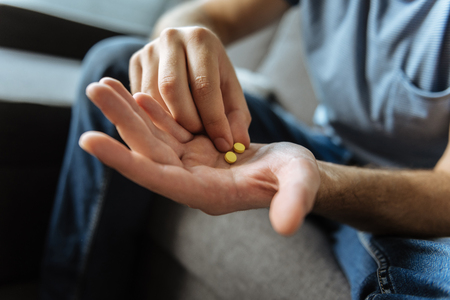 Selective focus of a palm of a cheerless ill man with two yellow pills