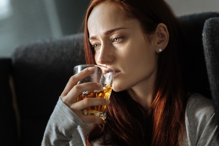 Unhappy moody woman drinking whiskyの写真素材
