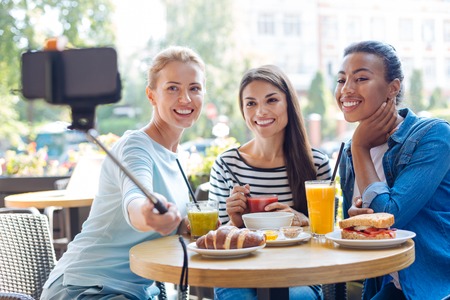 Charming women taking selfies with monopod in cafeの写真素材