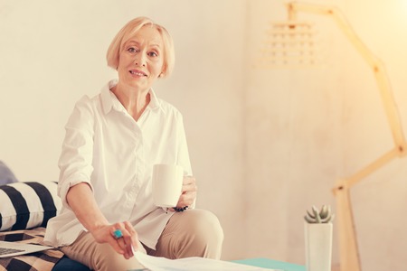 Positive beautiful aged woman drinking coffee