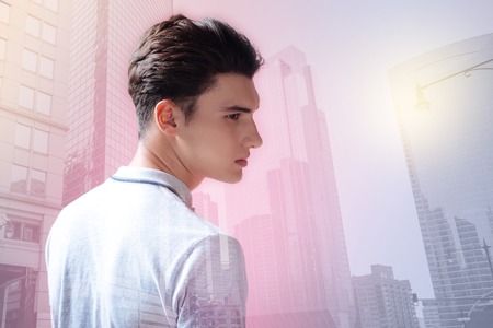 Handsome teenager looking away against city buildingsの写真素材