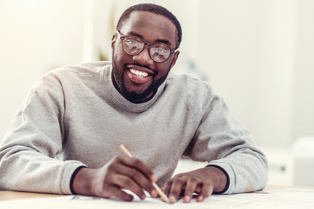 Beaming African American guy drawing and smiling into cameraの写真素材