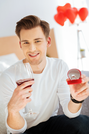 Happy young man holding engagement ring and drinking wineの写真素材
