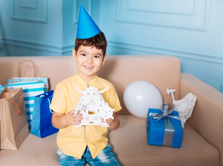Pleasant gift. Happy little boy sitting on the sofa full of presents and posing with a toy robot, his birthday giftの写真素材