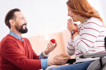 Be my wife. Joyful smiling bearded man making a proposal to an attractive alert blond handicapped...