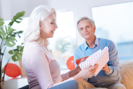 Side view on an excited elderly woman sitting next to her husband and smiling while looking at her gift.の写真素材