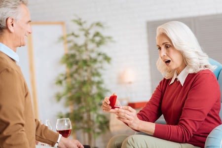 Amazed retired woman keeping her mouth wide opened after receiving a gift from her soulmate and looking at the ring.の写真素材