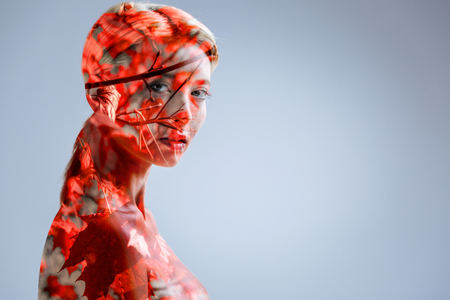Attractive young woman turning her head and looking into the camera confidently while posing against autumnal background.の写真素材