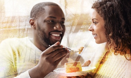 Close up of African American holding a fork with dessert while looking at his woman and smilingの写真素材