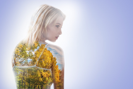 Thoughtful nice dreamy woman standing against blue background and thinking about nature while being in love with autumn forestsの写真素材