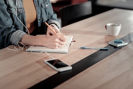 Useful notes. Smart attentive young student sitting and listening to a pleasant music while making notes in a big notebookの写真素材