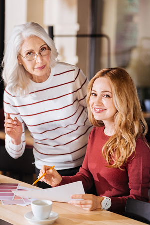 Clever designers. Calm creative responsible designers looking glad while being at the table and discussing all the details of their new project with a cup of coffee and bright color palettesの写真素材