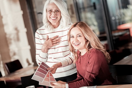 Beautiful colors. Cheerful emotional creative designers looking happy and laughing while choosing an appropriate color from three color palettesの写真素材