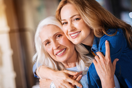 Close relatives. Positive attentive woman showing her respect and love to a kind loving grandmother while hugging herの写真素材