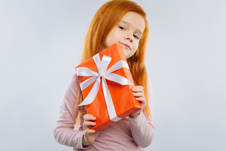 It is mine. Delighted kid pressing lips and holding box while looking straight at cameraの写真素材