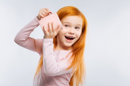 It is mine. Charming girl keeping smile on her face and looking aside while standing over grey backgroundの写真素材