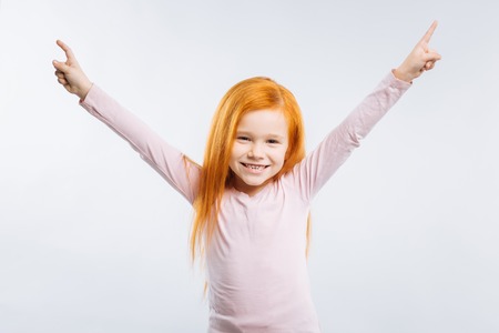 I am pleased. Smiling kid keeping smile on her face and holding hands up while looking straightの写真素材