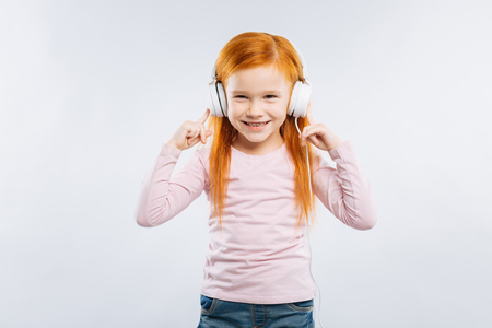My device. Cheerful girl keeping smile on her face and looking forward while standing isolated on grey backgroundの写真素材