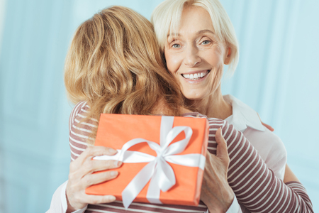 Generous present. Emotional cheerful senior woman feeling excited and happy after getting a wonderful present from her attentive caring granddaughterの写真素材