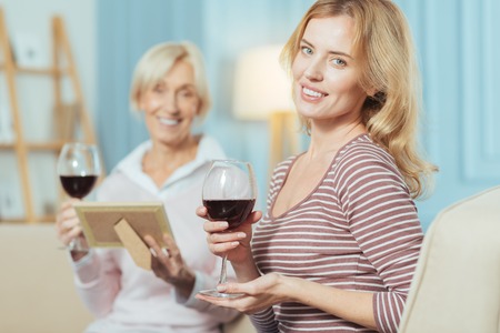 Beautiful glasses. Pleasant delighted women of different age sitting together and having a good time while holding the glasses full of red wineの写真素材