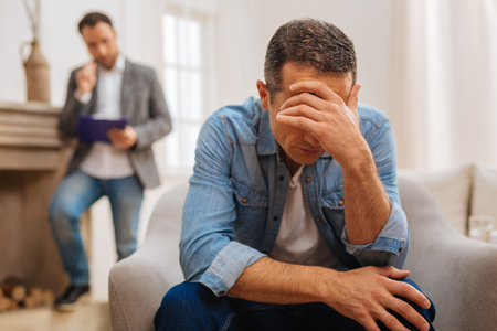 No more secret. Unhappy troubled male patient hiding his face behind his hand and crying while posing against the blurred backgroundの写真素材