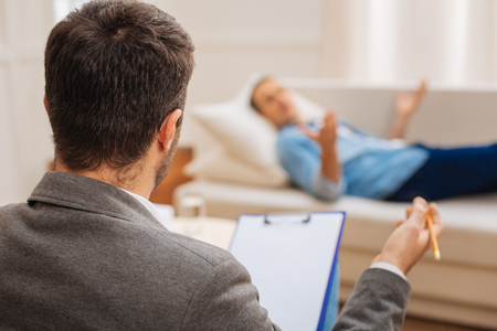 Patient world. Skillful experienced male doctor sitting and  listening about patient life while he relaxing on the couchの写真素材
