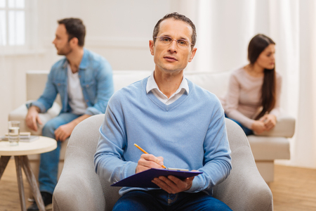 Useful job. Pleasant appealing male psychologist performing his job well when arguing couple deciding to visit himの写真素材