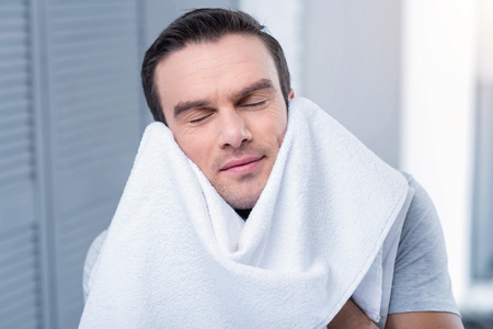 Shiny morning. Pleasant cheerful glad man wiping with towel and enjoying and closing his eyesの写真素材