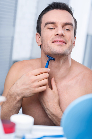 Very careful. Concentrated earnest good looking man removing bristles from his neck by using razor and looking downの写真素材