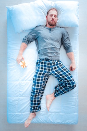 From her. Handsome bearded man making fist while keeping left leg bent in knee and sleeping after hard workの写真素材