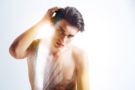 Nice pose. Pleasant attractive young man looking at you and holding his hand up while fixing his hairの写真素材