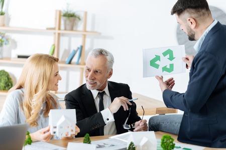 Important information. Clever progressive experienced engineers looking interested in protecting the earth while sitting in their office and discussing the houses made of recycled materialsの写真素材