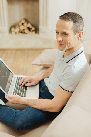 Confident glance. Young skilled professional worker looking into the distance and feeling confident while sitting on a sofa with a modern laptop on his kneesの写真素材