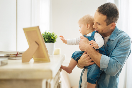 Touching things. Smart responsible kind father showing his curious interested baby many lovely items on the fireplace while making a small excursion in a houseの写真素材