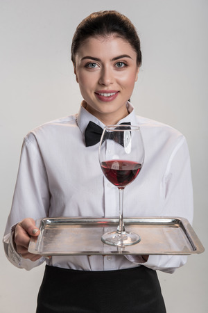 Red wine. Charming optimistic good looking woman smiling and stretching salver where glass of wine standingの写真素材