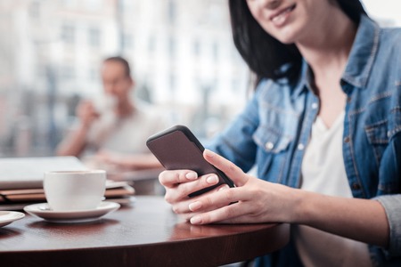 Online chatting. Cheerful female person expressing positivity and looking downwards while typing messageの写真素材