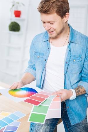 Bright colors. Positive emotional professional designer feeling satisfied while sitting in his comfortable office and looking at bright beautiful color palettesの写真素材