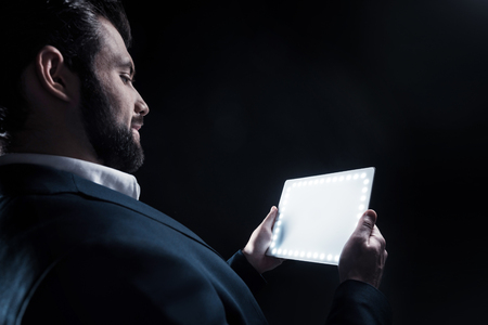Modern device. Cheerful positive smart businessman smiling and looking at his tablet while holding itの写真素材