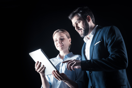 Professional businesspeople. Handsome smart bearded businessman standing together with his colleague and looking at the tablet screen while using modern technologyの写真素材