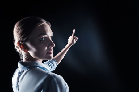 Futuristic technology. Pleasant nice young woman turning her head and looking at you while holding her hand in front of herの写真素材