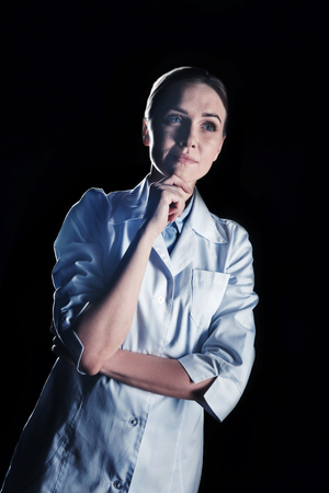 Interesting job. Pleasant thoughtful female scientist wearing labcoat and thinking about her job while holding her chinの写真素材