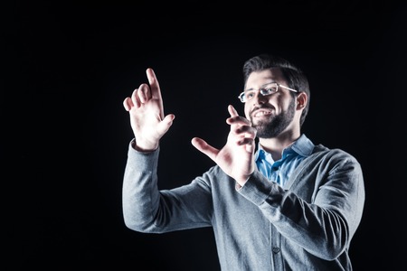 Positive emotions. Cheerful nice bearded man smiling and holding his hands up while using new technologiesの写真素材