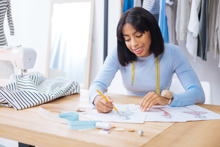 Beautiful drawings. Cheerful professional young worker of an atelier feeling satisfied while looking...