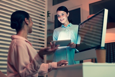 Nice chat. Beautiful young woman standing next to her female colleague and chatting with her while holding a tabletの写真素材