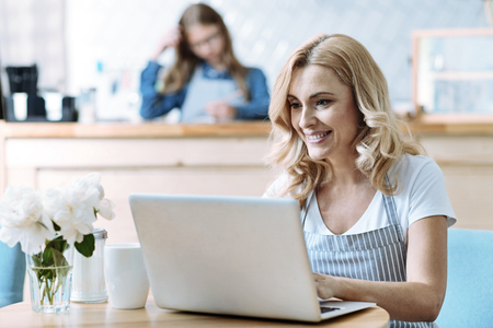 Cheerful woman keeping smile on her face and sitting in her cafe while having breakの写真素材