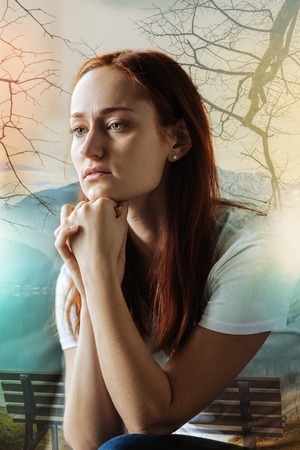Serious thoughtful redhead woman sitting in the room holding hands near head and looking aside.